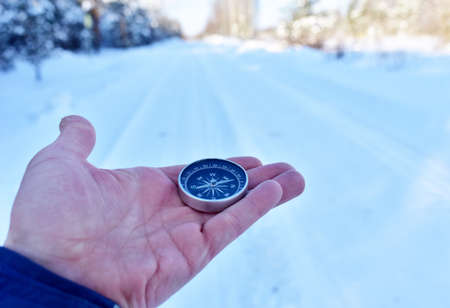 Compass in hand on snow background. Orientation on terrain in forest and mountain in winter time. Map reading and land navigation concept. Tourist compass and magnetic declination Ñalculatorの写真素材
