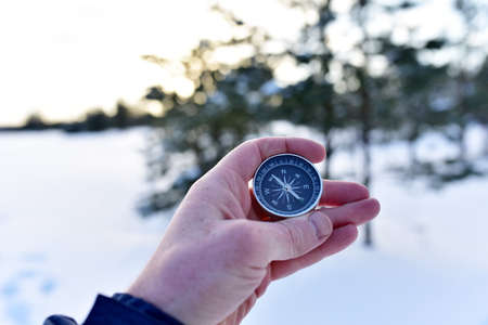Compass in hand on snow background. Orientation on terrain in forest and mountain in winter time. Map reading and land navigation concept. Tourist compass and magnetic declination Ñalculatorの写真素材