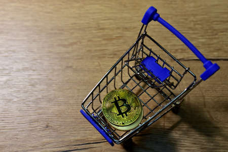 Shopping cart with bitcoin gold crypto coins on wood background. BTC cryptocurrency investing...