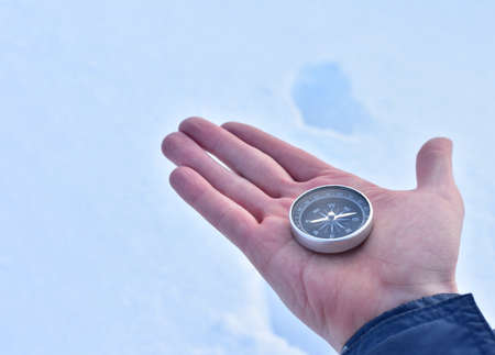 Compass in hand on snow background. Orientation on terrain in forest and mountain in winter time. Map reading and land navigation concept. Tourist compass and magnetic declination Ñalculatorの写真素材