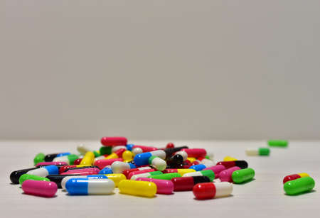 Colored pills in capsules on white wooden background. Pharmaceutical capsule and medical tablets. Medical pill for improving health. Concept of healthcare and medicineの写真素材