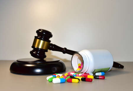 Mallet of judge and Multicolored pills in capsules in courtroom. Litigation Medicine-Related Healthcare in Pharmaceuticals. Justice concept. Judge hammer on law theme and legal systemの写真素材