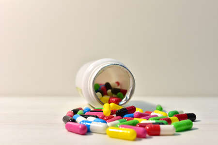 Colored pills in capsules from a bottle on white wooden background. Pharmaceutical capsule and medical tablets. Medical pill for improving health. Concept of healthcare and medicineの写真素材
