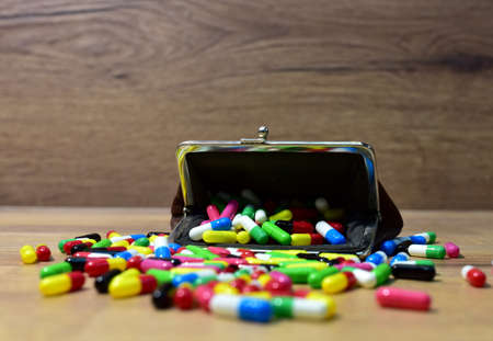 Pills in wallet on wooden background. Multicolored pharmaceutical pills, medical tablets and...