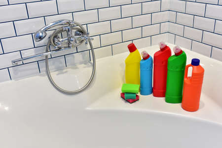 Detergent and sponge in bathroom on background of white tiles. Detergents bottles and kitchen sponges. Household chemicals cleaning of the restroom. Anti-bacterial liquids for house clean and toiletの写真素材