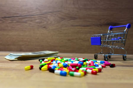 Pills in a shopping basket on a heap of American dollars. Economy concept of spending money on medicines and pills. Medical pill for maintaining and improving health in trolley. Shopping cartの写真素材
