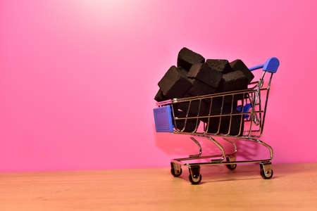 Charcoal in a shopping cart on a pink background. Coal sale or mining conceptの写真素材