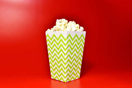 Popcorn in colored cardboard packaging. Heap of salted popcorn in paper striped bucketon a red background.の写真素材