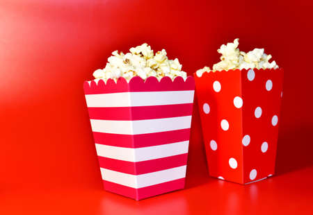 Popcorn in colored cardboard packaging. Heap of salted popcorn in paper striped bucketon a red background.の写真素材