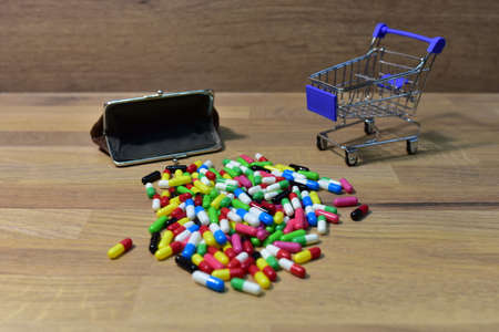 Pills with wallet at a shopping basket on wood backgrond. Economy concept of spending money on medicines and pills. Medical pill for maintaining and improving health in trolley. Shopping cartの写真素材