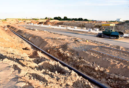 Asphalting the road and laying the sewer pipe at the construction site. Asphalt paver machine during...