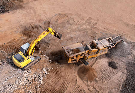 Excavator loading old concrete into stone jaw crusher. Stone crushing machine on landfill. Recycling...