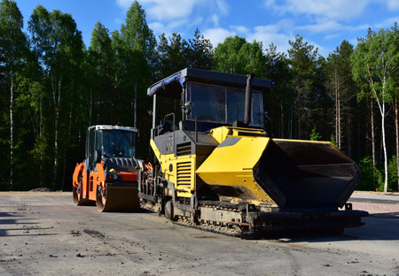 Asphalt paver machine during road work. Road roller at construction site for paving works. ered over...