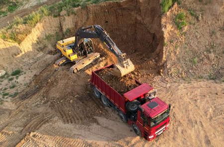 Excavator load the sand into dump truck. Aerial view of an backhoe on earthworks. Open pit...