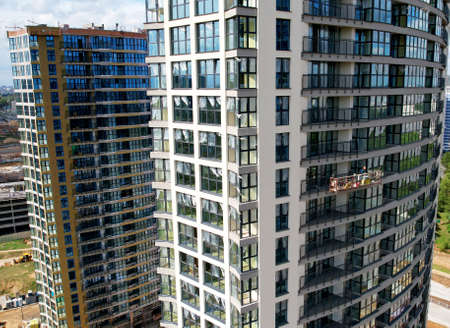 Suspended cradle for works of the facade of the skyscraper. Construction of multi-storey building. Mobile scaffolding platform for construction work at height and plastering and wall painting.の写真素材