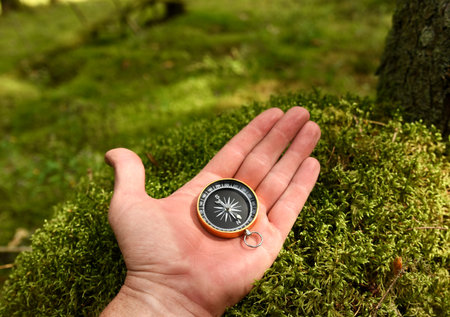 Compass in hand at forest. Tourist compass for orientation on the terrain. Magnetic declination Ñalculator. Historical explorer help. Map reading and land navigation concept. Orient on mapsの写真素材
