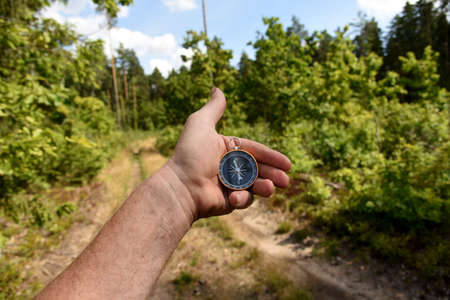 Compass in hand at road in the forest. Tourist compass for orientation on the terrain. Magnetic declination Ñalculator. Map reading and land navigation concept. Orient on mapsの写真素材