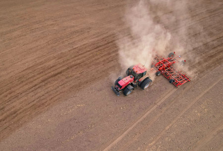 Soil Tillage in farmers country. Red Tractor on cultivating field work. Agricultural tractor on cultivation field for sowing seeds. Farming and seeding concept. Planting Equipment and Farm Machine.の写真素材