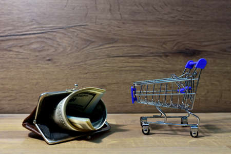 Money in a wallet with a shopping cart. Dollars in a bag for buying groceries and goods in the...