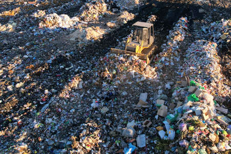 Landfill waste disposal. Garbage dump with waste plastic and polyethylene. Bulldozer at landfill working on rubbish disposal. Reduce greenhouse gas emissions and methane emissions.の写真素材
