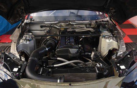 Sports car engine with turbine. An open race car hood on a pit stop while racing on a race track....