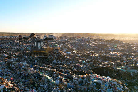 Garbage dump with waste plastic, polyethylene and food waste. Trash disposal for recycling and re-use. Bulldozer at landfill working on rubbish disposal. Dozer on a industrial landfill. Soft focus.の写真素材