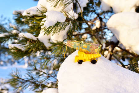 Toy truck with a Christmas ball on the background of white snow in the forest. oncept of preparing...