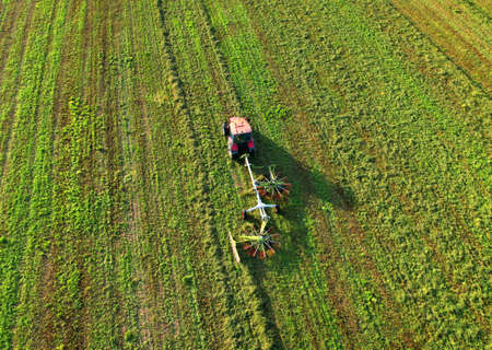 Tractor raking grass for silage harvesting. Agriculture farm machinery work at the field. cutting...