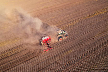 Tractor sowing seed on plowed field, drone view. Farming and seeding machinery for plowed field. Seed sowing in farm season. Planting Equipment for agriculture. Tractor at arable. Plowed crop field.の写真素材