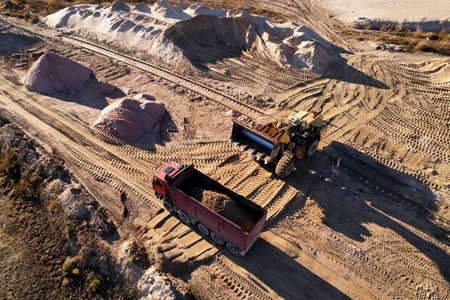 Wheel loader load the sand into dump truck in open pit. Developing the sand in the opencast. Heavy machinery on earthworks in quarry. Mining truck transports sand from open-pit mining, aerial view.の写真素材