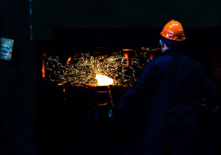 Blacksmith work with red hot iron under a press on metallurgical plant. Metal forging, stamping under hammer forge at workshop of forge factory. Blacksmithing, steelmaking and hot rolling mill.の写真素材