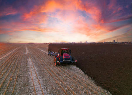 Tractor Plowing field on sunset. Cultivated land and soil tillage. Tractor with disc cultivator on land cultivating. Agricultural tractor on cultivation field. Tractor disk harrow on plowing field.の写真素材