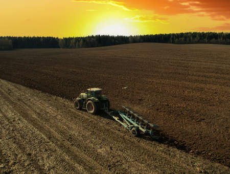 Tractor with plow on field cultivating. Green tractor plowing field on sunset. Cultivated land and soil tillage. Agricultural tractor on field cultivation. Tractor disk harrow on plowing, aerial view.の写真素材