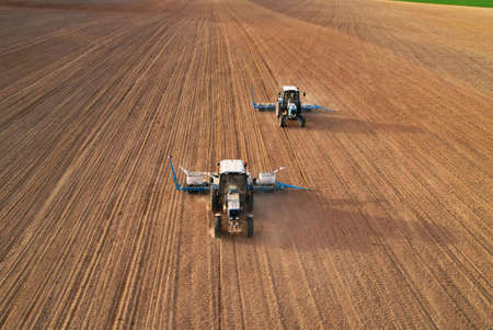 Tractor sowing seed on plowed field. Sowing seeds of corn and sunflower. Blue Tractor with disk harrow on plowing field. Seeding machinery on farm field. Seed sowing in farmland, aerial view.の写真素材