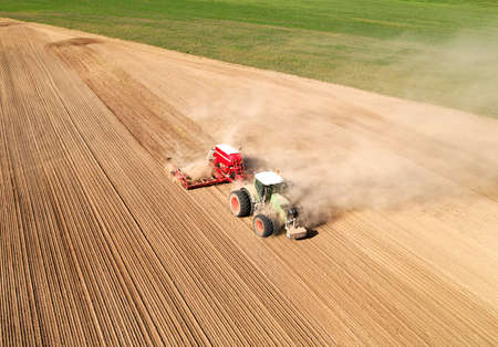 Tractor sowing seed on plowed field, drone view. Farming and seeding machinery for plowed field....