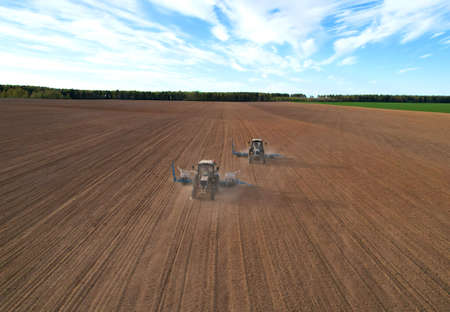 Tractor sowing seed on plowed field. Sowing seeds of corn and sunflower. Blue Tractor with disk harrow on plowing field. Seeding machinery on farm field. Seed sowing in farmland, aerial view.の写真素材