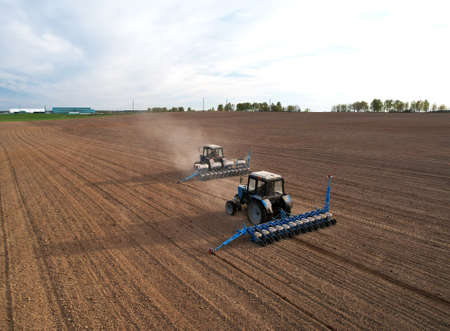 Tractor sowing seed on plowed field. Sowing seeds of corn and sunflower. Blue Tractor with disk...