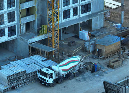Pouring concrete in bucket from mixer truck. Tower crane on formwork at construction site. Reinforced concrete. Civil engineering during formworks. Concrete transport mixing truck during built.の写真素材
