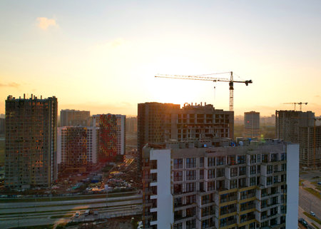 Crane during the construction of a residential building at sunset. Construction site at sunset with a tower crane and unfinished buildings and residential houses skyscrapers.の写真素材