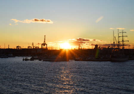 Silhouette of yachts and boats on sunset in the in La Marina de Valencia. Sunset at the port. Luxury yacht and fishing motorboat in yacht club at Mediterranean Sea. Skiff and Sailboat in harbor.の写真素材