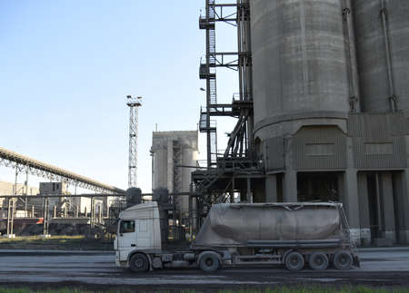 Truck with cement semi-trailer at cement plant site. Cement mix production at industrial factory....