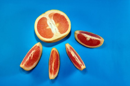 Grapefruit cut in half and into slices on a blue background
