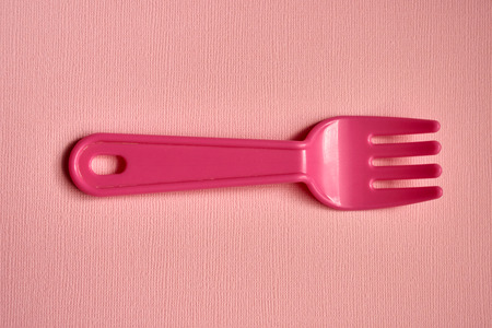 Close-up of one childish plastic pink forks on a pale pink background. Dishes for a picnic. Copy space with selective focus.の写真素材