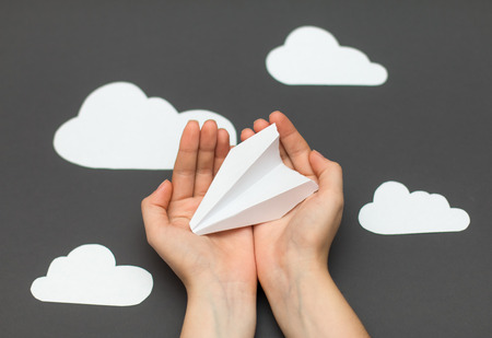 White paper airplane in hands and clouds on a gray backgroundの写真素材