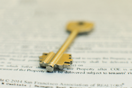 house key lying on a contract of house sale lease insurance or mortgage in a real estate concept viewed low angle with focus to the tip.の写真素材