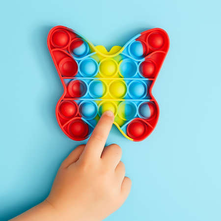 Trendy toy antistress. Anonymous child with colorful poppit game. Image of trendy Pop it fidget toy. Top view of the new sensory toyの写真素材