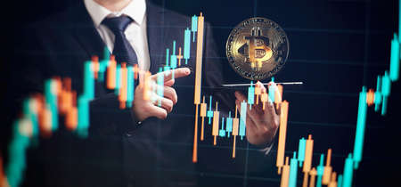 Smartphone with bitcoin trading chart. Holding in hand a gold Bitcoin Cash coin. Trading on the cryptocurrency exchange.の写真素材