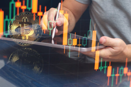 Man bitcoin trading chart on the screen. Holding in hand a gold Bitcoin Cash coin. Trading on the cryptocurrency exchange.の写真素材