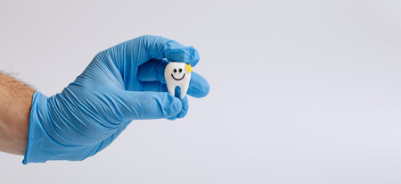 Hand in blue glove holding a tooth model with a smiley