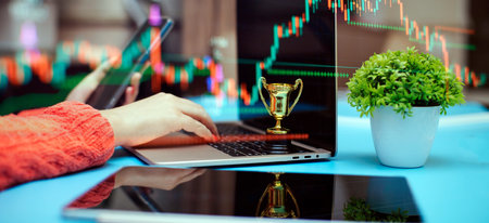 Close up of businesswoman using laptop computer and holding trophy cup on table with forexの写真素材